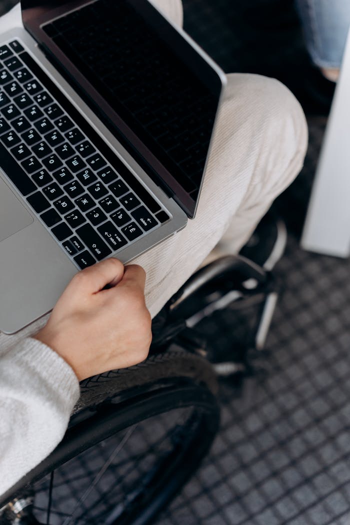 A close-up shot of a laptop being used by a person in a wheelchair, indoors.